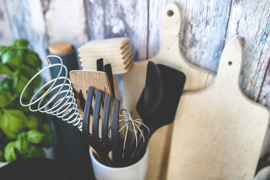 Collection of kitchen utensils including spatula, whisk, and chopping boards against a rustic background.
